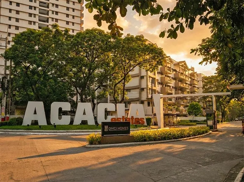 The Acacia Estates entrance signage in Taguig at golden hour, with mid-rise buildings and mature trees behind it.