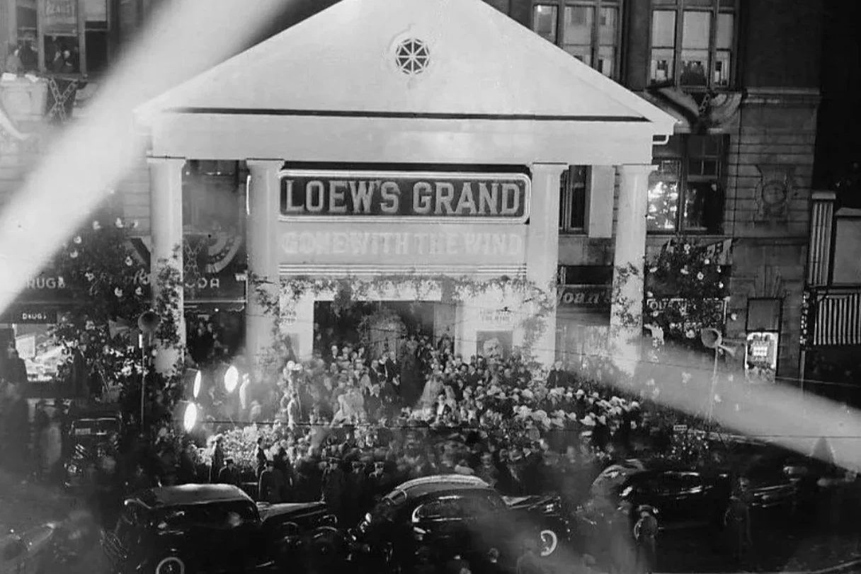 Black-and-white night photograph of a crowd packed outside Loew's Grand Theatre in Atlanta for the 1939 world premiere of Gone with the Wind, its columned entrance lit up with the title and spotlights crossing the frame.